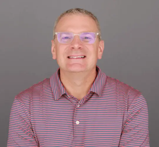 t.mcmillan headshot headshot of a man smiling with clear glasses wearing a striped polo shirt.